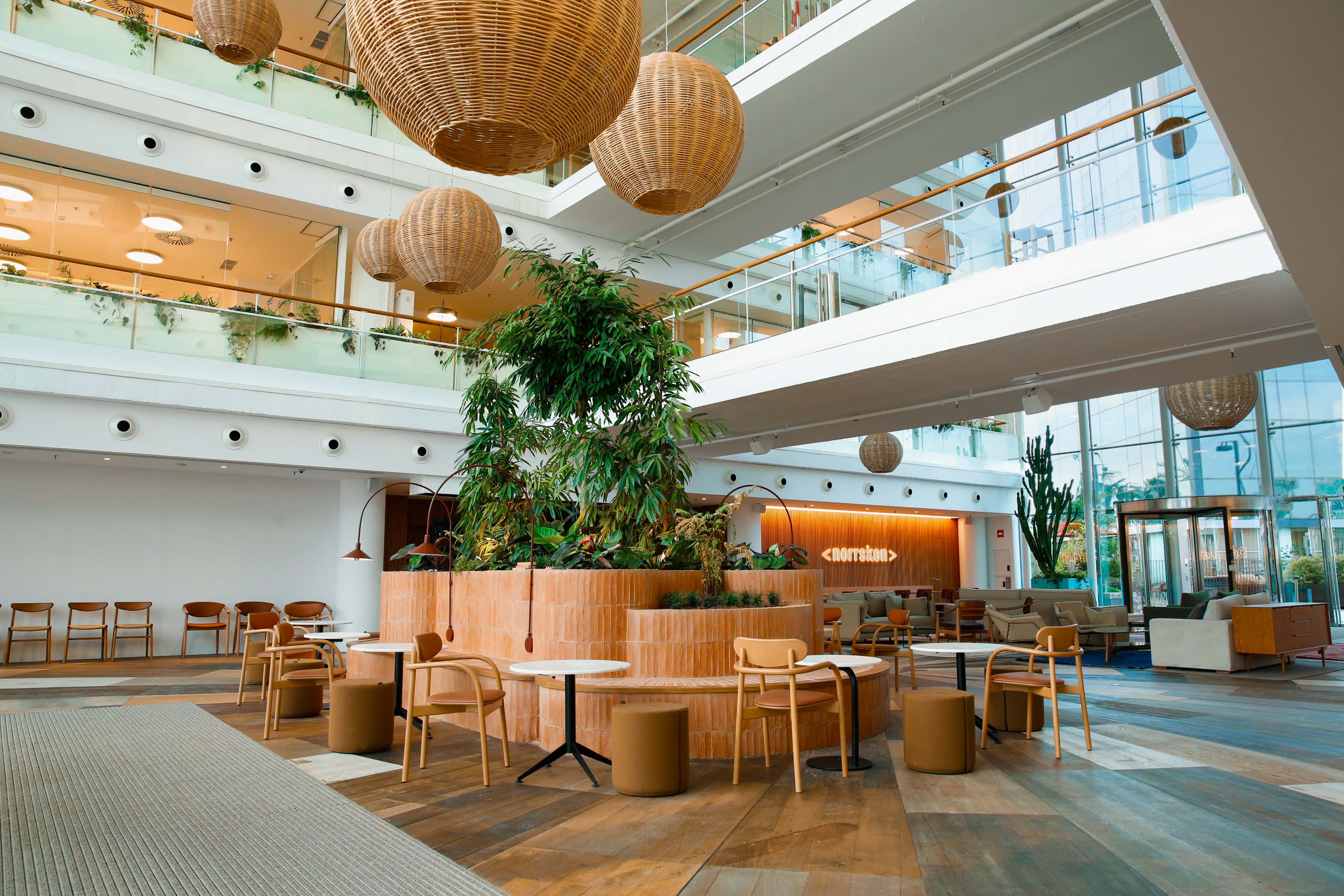 The Norrsken House Barcelona atrium with woven pendant lights, central greenery, and the Norrsken sign on the wooden back wall.